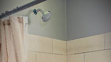 A shower with a tiled wall, a showerhead, and a drain.
