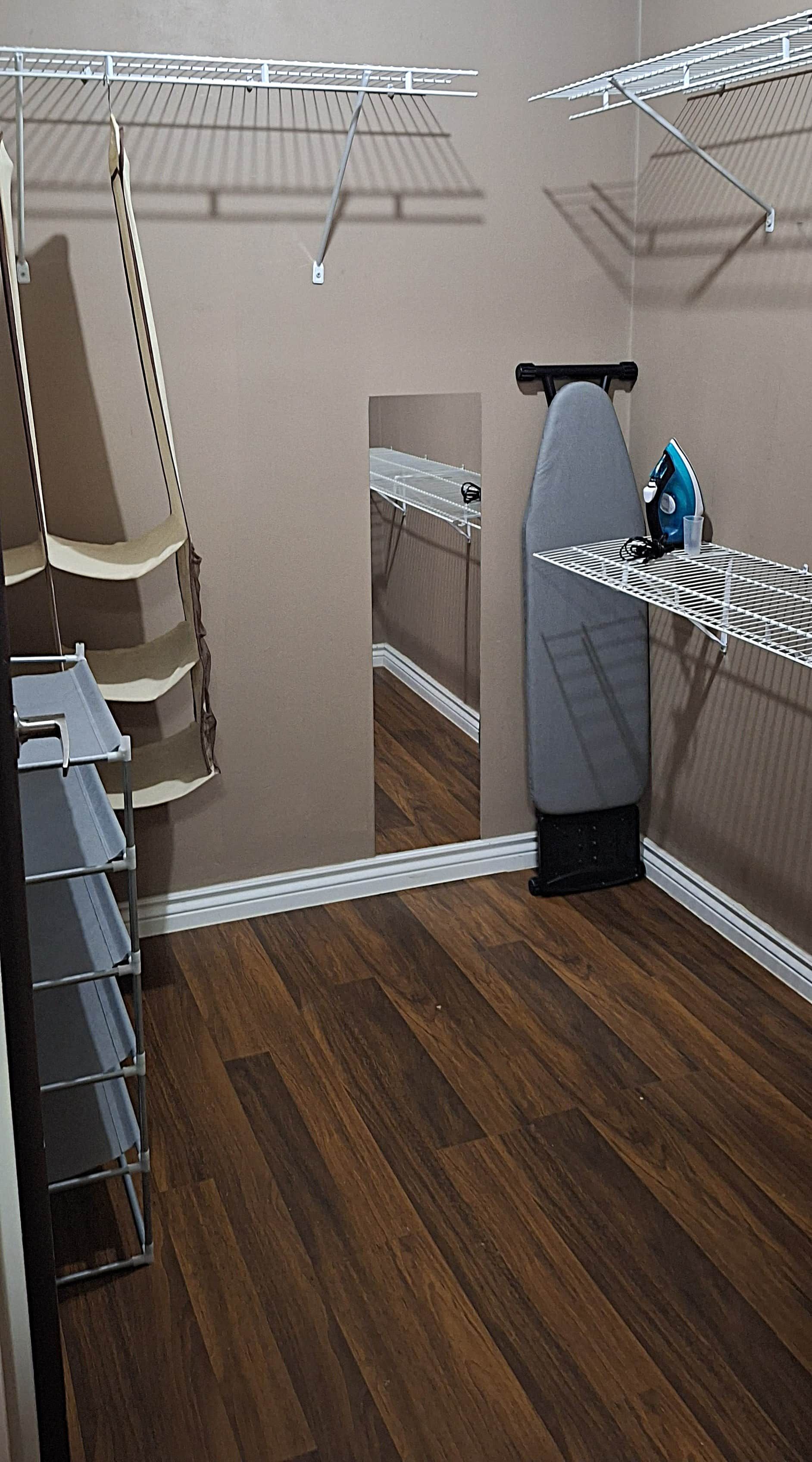 A laundry room with a drying rack, an ironing board, and a blue iron.