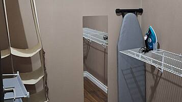 A laundry room with a drying rack, an ironing board, and a blue iron.
