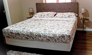 A bed with a patterned bedspread, two bedside lamps, and a wooden headboard. - Akim's Apartments (Scarborough)