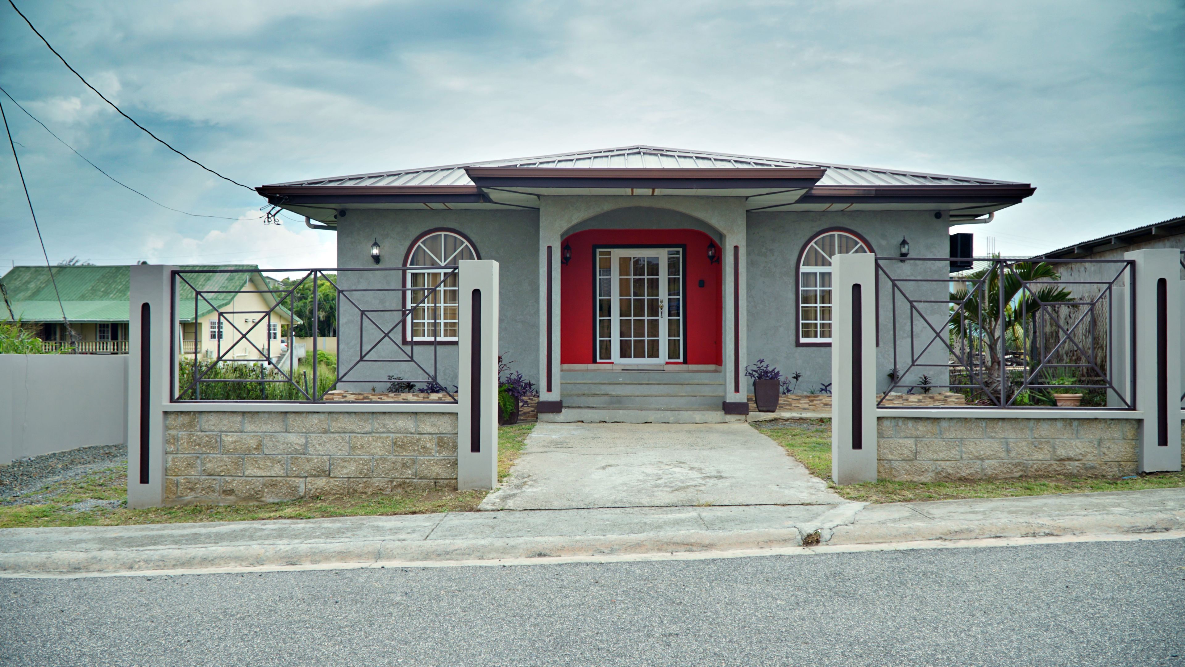 A residential house with a red door, a front porch, and a gated entrance.