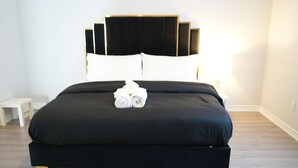 A neatly made bed with a black bedspread and white pillows, a small bedside table, and a lamp on the right side. - Charming GTA Retreat| Near Airport and Wonderland (Brampton)