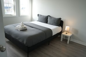 A modern bedroom with a bed, a bedside table with a lamp, and a window. - Charming GTA Retreat| Near Airport and Wonderland (Brampton)