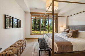 Ein Schlafzimmer mit einem Himmelbett, einer Bank und einem großen Fenster mit Blick auf Bäume.