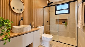 A modern bathroom with a round mirror, a freestanding sink, a toilet, and a glass-enclosed shower area. - LOFT 10 (Vinhedo)