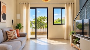 A modern living room with a sofa, TV, and a balcony with a view of greenery. - LOFT 10 (Vinhedo)