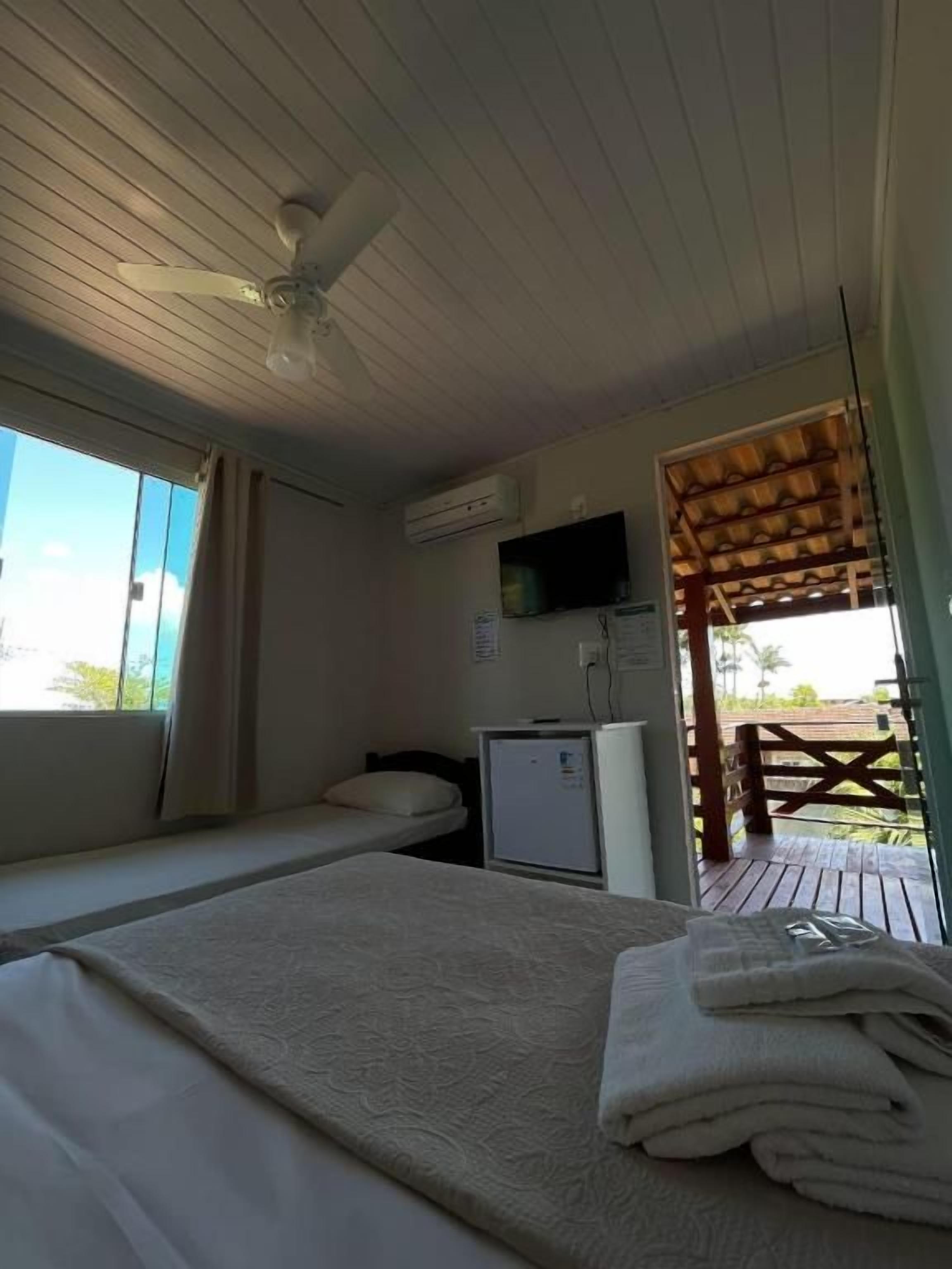 Quarto com cama, escrivaninha, televisão e janela.