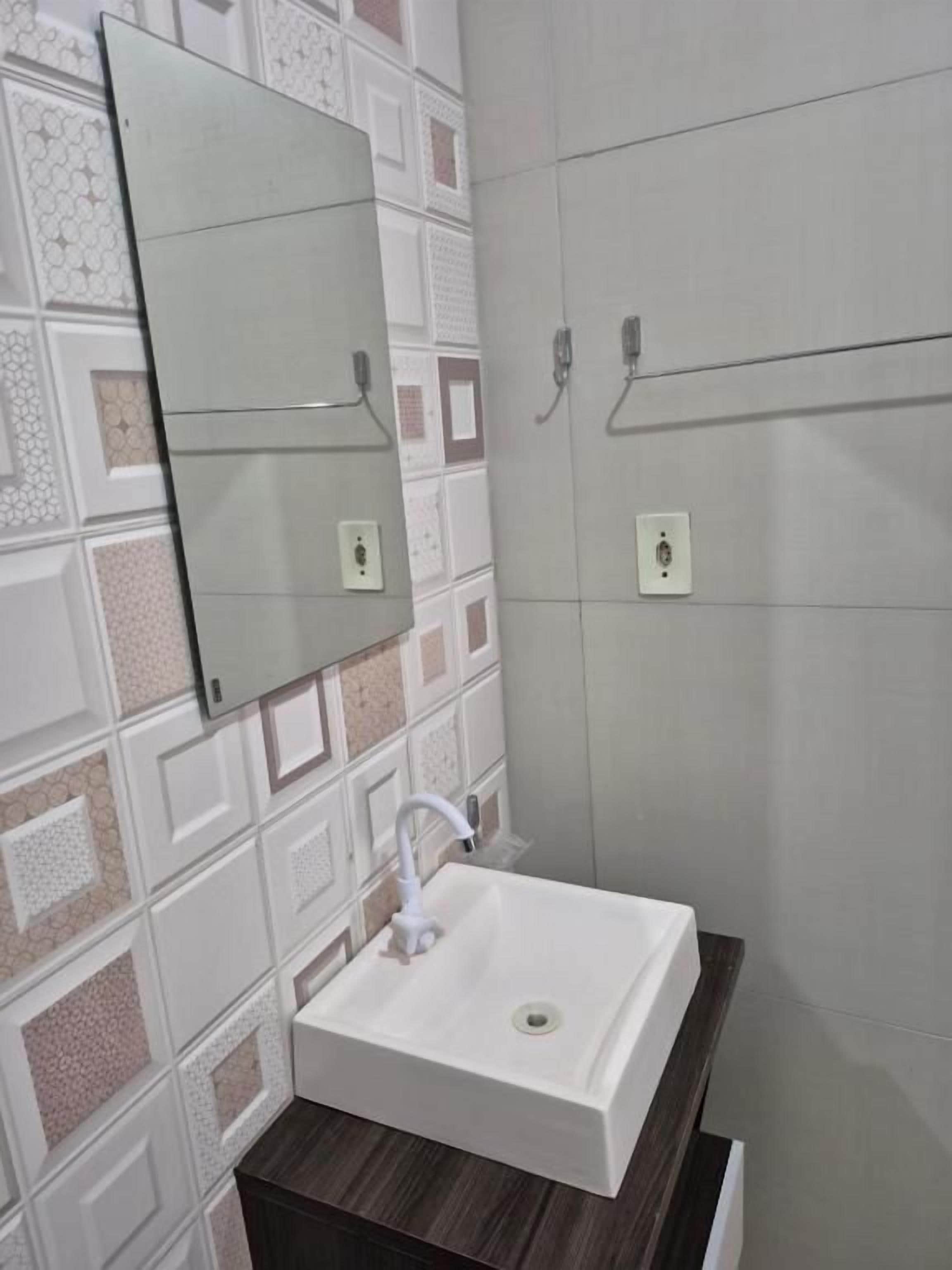 Casa de banho com lavatório branco, espelho e suporte para toalhas.