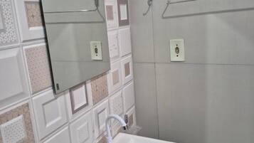 Casa de banho com lavatório branco, espelho e suporte para toalhas.