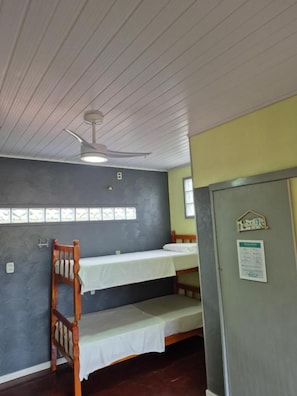 Een slaapkamer met stapelbed, plafondventilator, raam met zonwering en een deur met een bordje.
