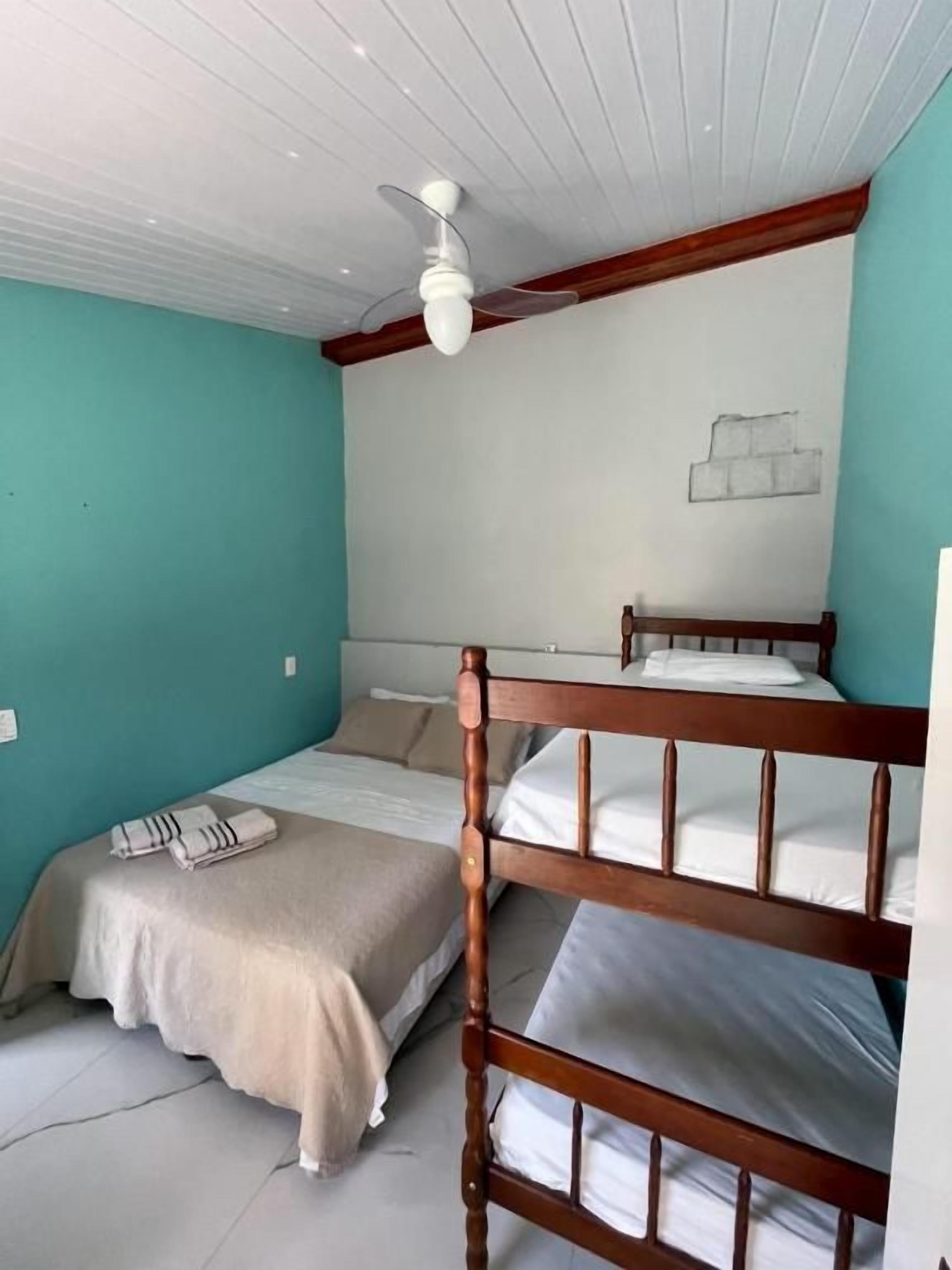 A single bedroom with a bunk bed, a ceiling fan, a bed with a beige blanket, and a wall with a simple drawing.