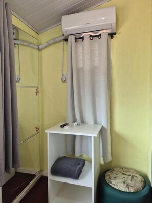 Een badkamer met een wit schap, een handdoek, een groene kruk en een douchegordijn.