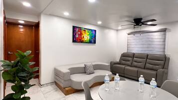 A modern meeting room with a round table, grey chairs, a sofa, and a ceiling fan.