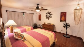 A hotel room with two beds, a ceiling fan, a standing fan, a decorative wall piece, and a lamp. - Where Tropical Gardens Meet Poolside Paradise—Villa Jenny (Manzanillo)
