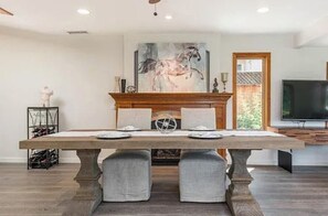 A dining area with a wooden table, two grey upholstered chairs, a fireplace, and a large painting on the wall. - Beautiful 2-bedroom house with AC in charming Santa Barbara (Santa Barbara)