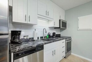 A modern kitchen with stainless steel appliances, white cabinetry, and a marble countertop.
