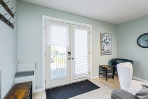 A room with a double door, a bench, a chair, a small table, and a clock on the wall.