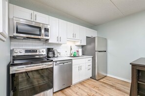 A compact kitchen with white cabinetry, stainless steel appliances, and a wooden floor. - K's Condominium - Minutes to Ski, Trails, Shops, Beach (Collingwood)