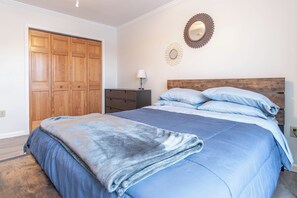 A bedroom with a large bed, a wooden wardrobe, a nightstand, and a wall-mounted mirror. - 3-bedroom townhome in soothing Sackets Harbor with AC (Sackets Harbor)