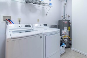 A laundry area with two front-loading washers and dryers, a water heater, and a hose connected to the wall. - 3-bedroom townhome in soothing Sackets Harbor with AC (Sackets Harbor)