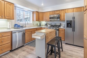 A modern kitchen with wooden cabinets, stainless steel appliances, and a built-in island with stools. - 3-bedroom townhome in soothing Sackets Harbor with AC (Sackets Harbor)