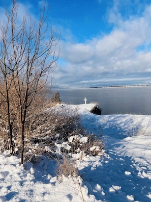 A snowy landscape with a body of water, a cross, and leafless trees. - 3-bedroom townhome in soothing Sackets Harbor with AC (Sackets Harbor)