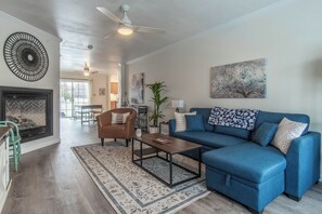 A living room with a blue sofa, a brown armchair, a coffee table, a fireplace, and a ceiling fan. - 3-bedroom townhome in soothing Sackets Harbor with AC (Sackets Harbor)