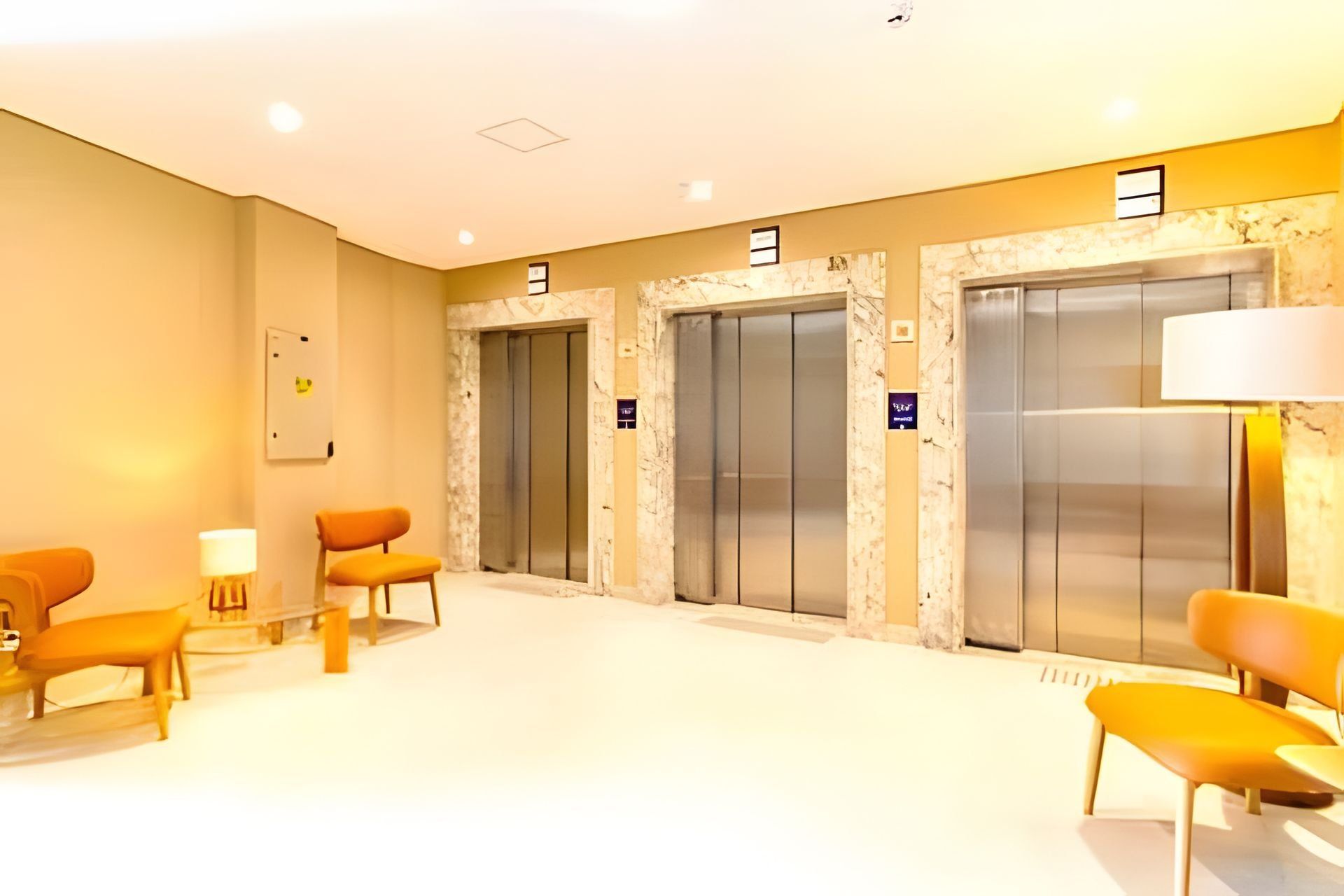 A hotel lobby with three elevators, a reception desk, and seating areas.