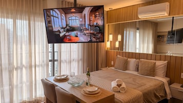Una habitación de hotel con cama, mesita de noche, televisor y cortinas.