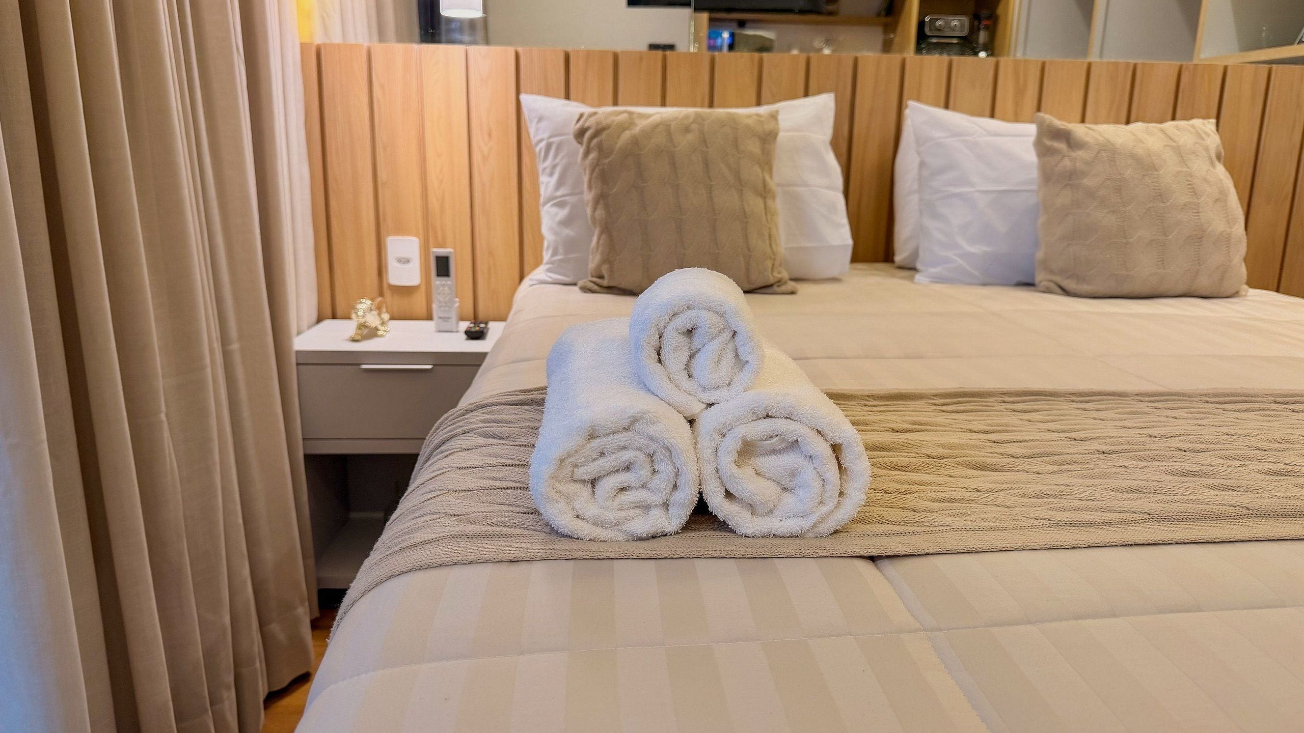 A hotel room with a neatly made bed, a bedside table with a lamp, and a wall-mounted TV.