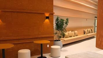 Un intérieur moderne avec un mur en briques, un coin salon avec des coussins et trois tables rondes.