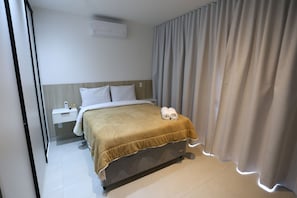 Una habitación de hotel con cama, mesita de noche, panel de control y cortina.