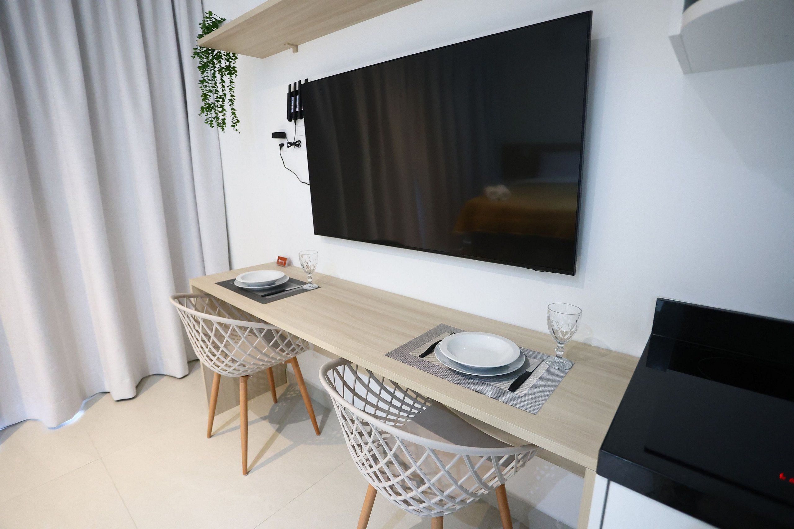 Uma área de refeições moderna com uma mesa de madeira, duas cadeiras brancas e uma televisão de tela plana grande fixada na parede.