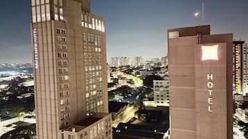A hotel building with a prominent 'HOTEL' sign, surrounded by high-rise buildings and a cityscape at dusk.