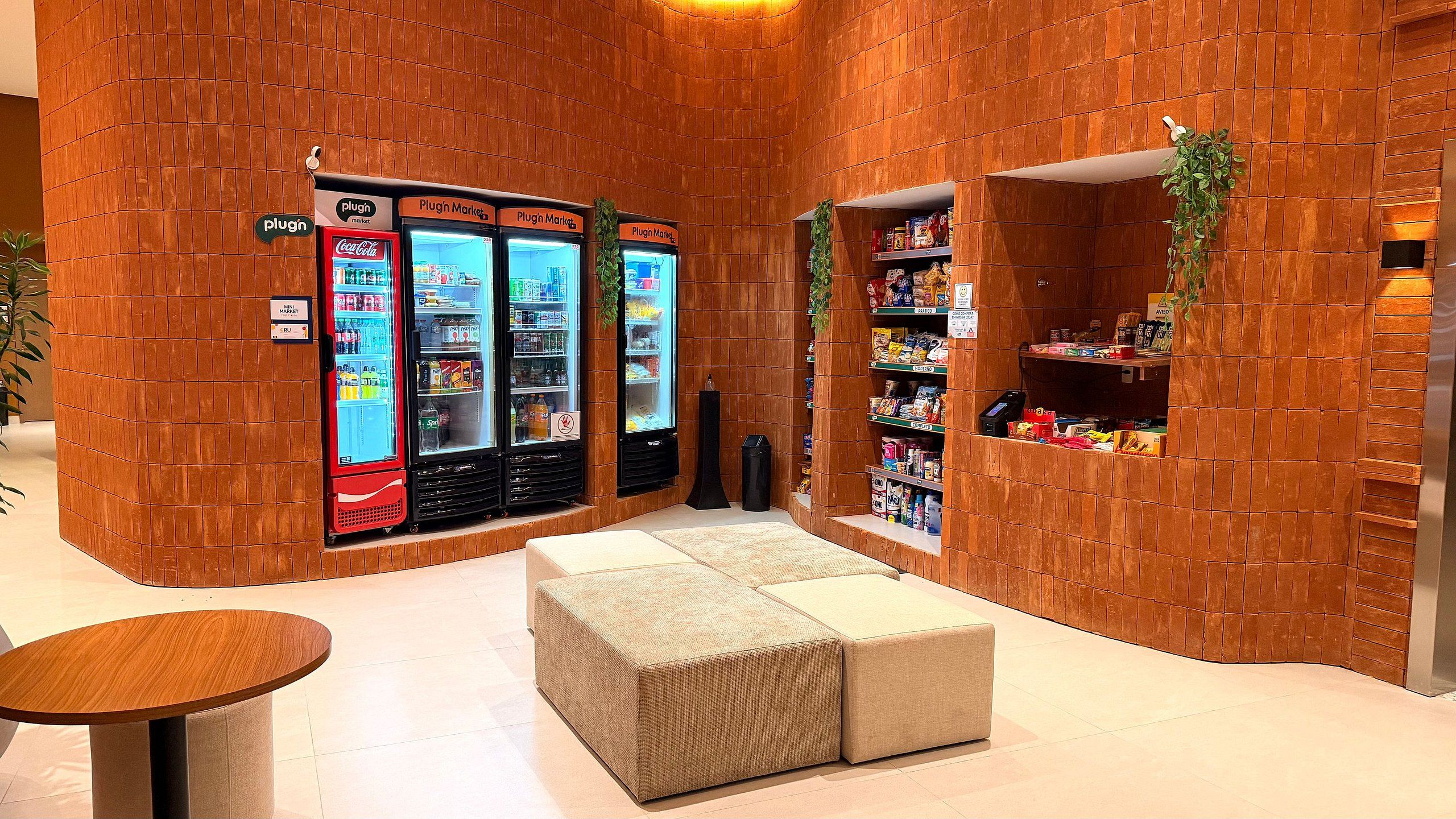 A room with a brick wall, a Coca-Cola refrigerator, a mini market, and a seating area.