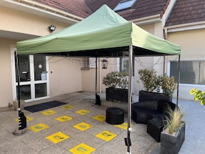 Un espace extérieur abrité, doté d’une pergola verdoyante, de plantes en pot et d’un sol carrelé orné de motifs jaunes.