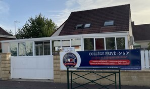 Une entrée privée menant à un établissement d’enseignement supérieur, avec une enseigne, un portail et un bâtiment doté d’un toit en pente.