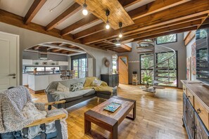 A spacious living area with a wooden ceiling, a kitchen in the background, and a spiral staircase leading to an outdoor area. - La maison aux Hibiscus - Jardin - Wifi (Saint-Denis)