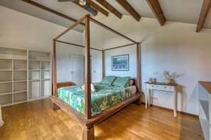 A four-poster bed with a green leaf-patterned bedspread, a white door, a small bedside table with a lamp, and a wall-mounted picture. - La maison aux Hibiscus - Jardin - Wifi (Saint-Denis)