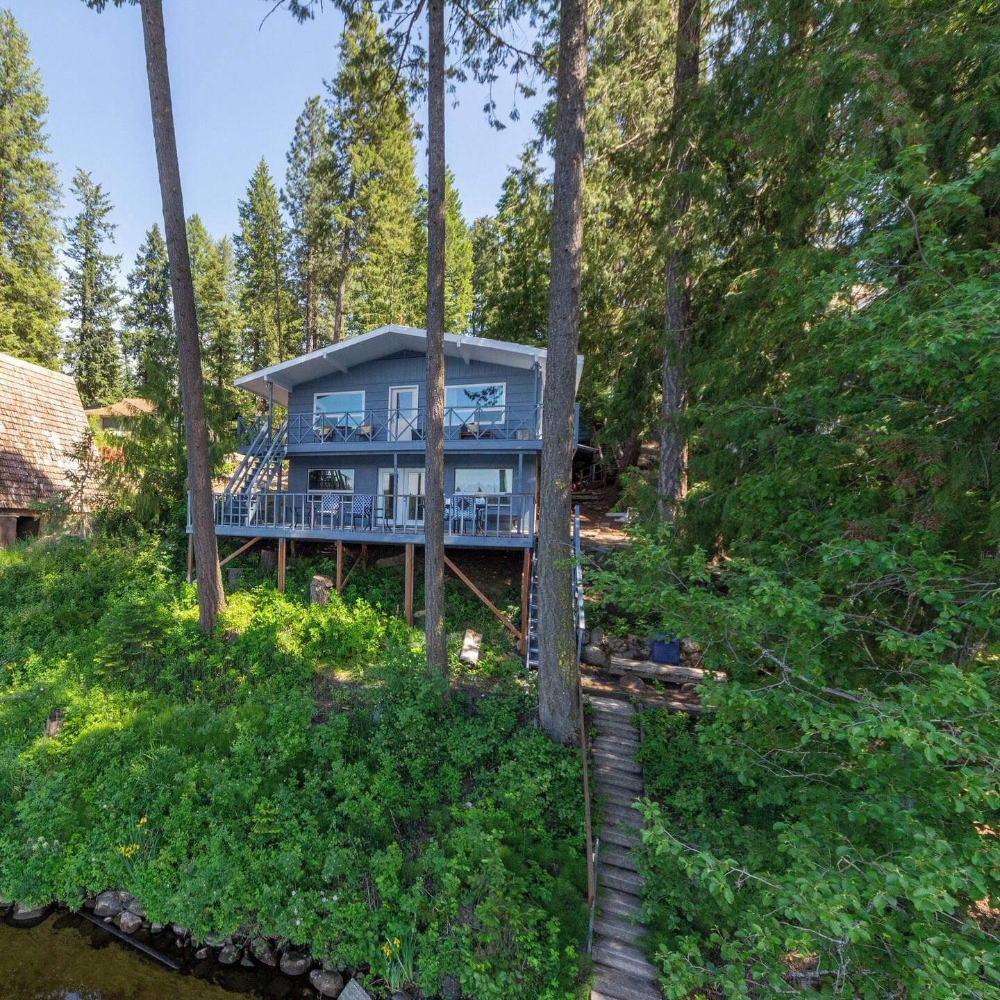 A two-story cabin with a deck, surrounded by dense forest.