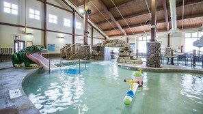 Ein Hallenbad mit Wasserrutsche, Froschstatue und Wasserspielplatz.