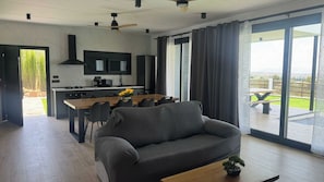 Ein modernes Wohnzimmer mit einer Couch, einem Couchtisch und Blick auf eine Terrasse mit Tisch und Stühlen.
