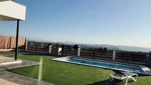 A backyard with a swimming pool, a grassy area, and a view of distant mountains.