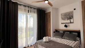 A bedroom with a bed, a ceiling fan, a window with curtains, and a wall-mounted light fixture.
