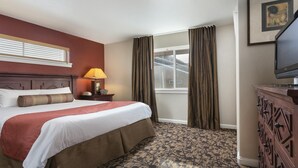 A hotel room with a large bed, a bedside lamp, a dresser, a window with curtains, and a television. - Steamboat Springs Ski Escape with Hot Tubs & Spacious 2BR Deluxe Stay (Steamboat Springs)