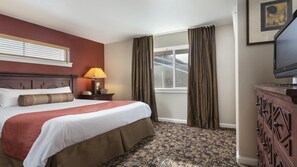 A hotel room with a large bed, a bedside lamp, a dresser, a window with curtains, and a television. - Steamboat Springs Ski Escape with Hot Tubs & Spacious 2BR Deluxe Stay (Steamboat Springs)