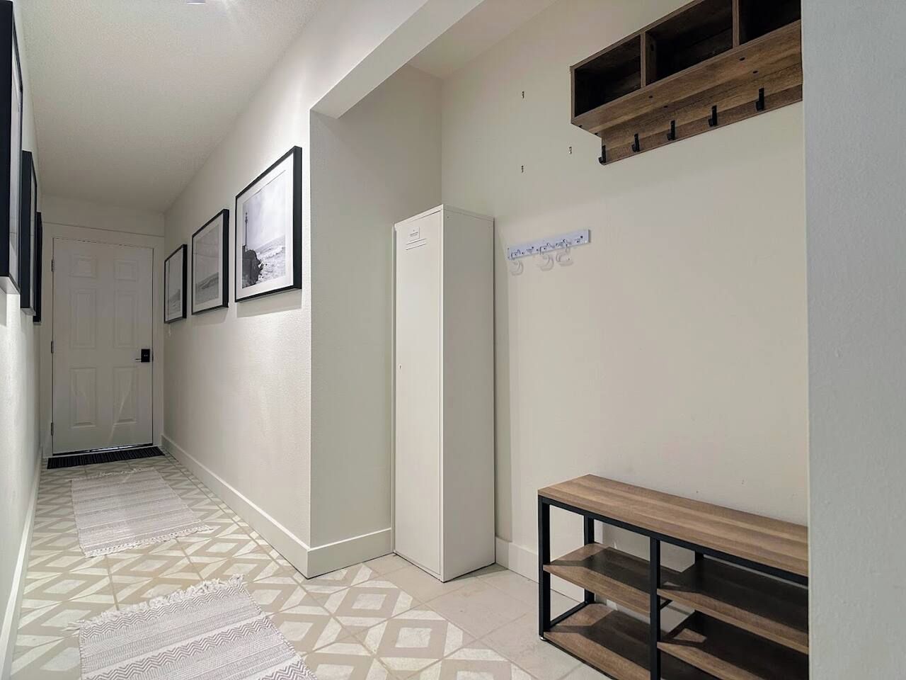 A hallway with a patterned floor, a white door at the end, and a bench with a wooden top and metal frame.
