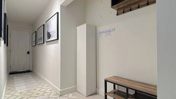 A hallway with a patterned floor, a white door at the end, and a bench with a wooden top and metal frame.