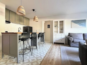 A modern kitchen with a bar area, a dining table with chairs, a sofa, and a cabinet with glass doors. - Resting Beach Place | Luxurious Beachfront Condo (Neskowin)