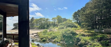 A view from a covered outdoor area overlooking a natural landscape with a stream, trees, and a distant beach.